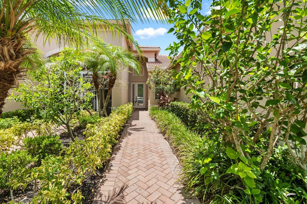 A brick walkway leads to the front entrance of a house surrounded by lush landscaping — 15665 AURORA LAKE CIRCLE, WIMAUMA, FL
