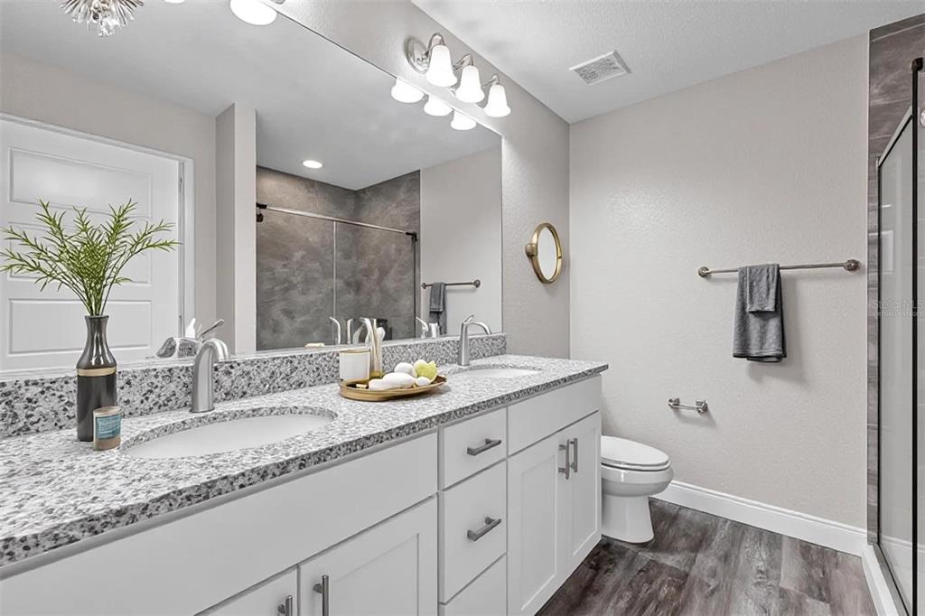A modern bathroom features a double vanity with granite countertops, white cabinets, and a large mirror — 17 CEDAR TREE RUN, OCALA, FL