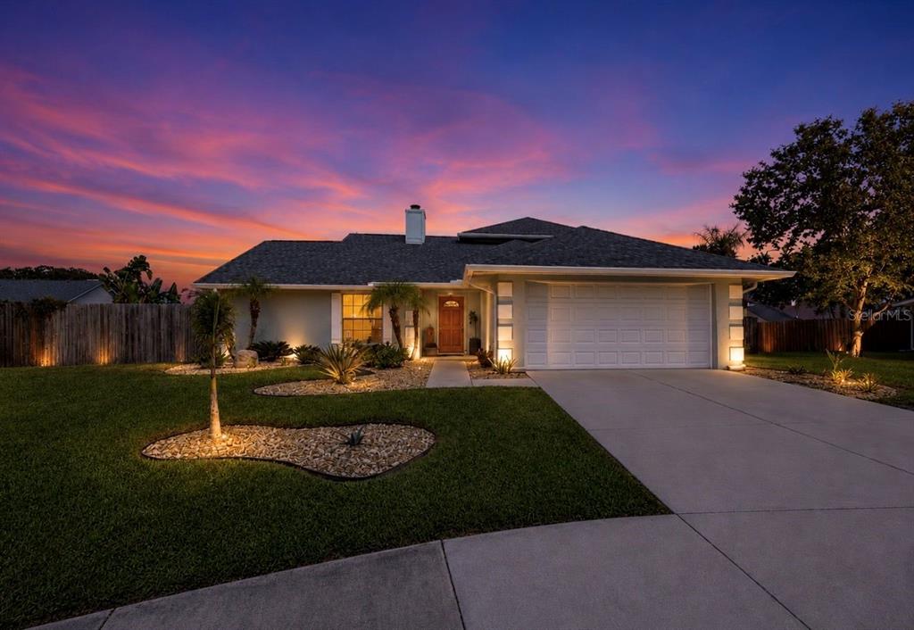 A single-story house with a white garage, a wooden front door, and illuminated landscaping at dusk — 1921 STANFIELD DRIVE, BRANDON, FL