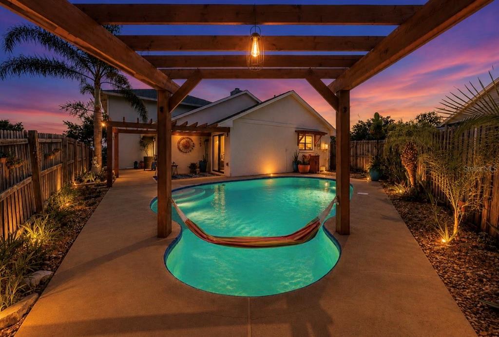 A backyard features a swimming pool, a wooden pergola with a hammock, and exterior lighting — 1921 STANFIELD DRIVE, BRANDON, FL