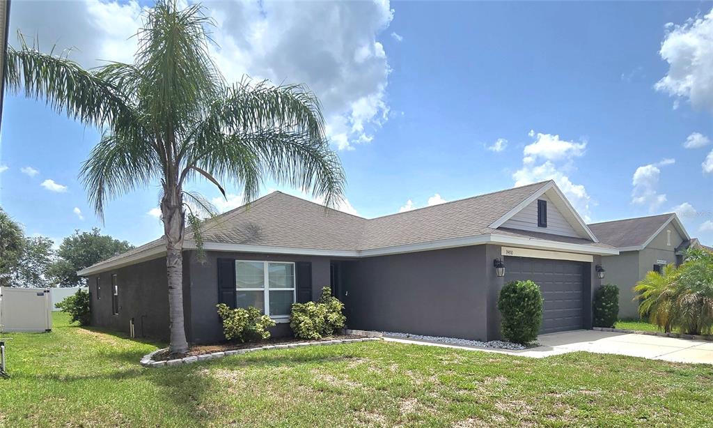 A single-story house with dark gray exterior walls, a two-car garage, and a palm tree — 14450 HADDON MIST DRIVE, WIMAUMA, FL