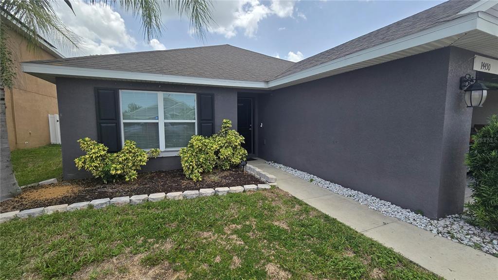 The exterior of a single-story house features dark gray stucco walls and a front walkway — 14450 HADDON MIST DRIVE, WIMAUMA, FL