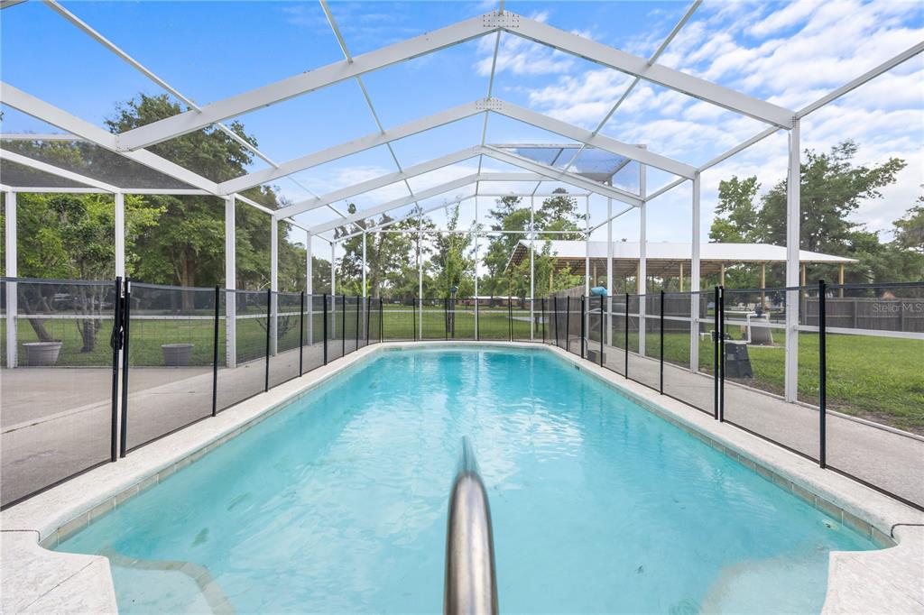 A rectangular swimming pool is enclosed by a white screen cage and a safety fence — 1005 11TH AVENUE, WELLBORN, FL