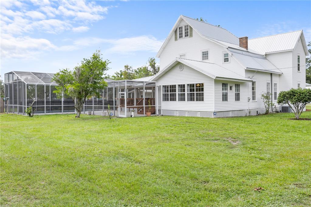 A white two-story house with a metal roof and an attached screened-in pool enclosure — 1005 11TH AVENUE, WELLBORN, FL