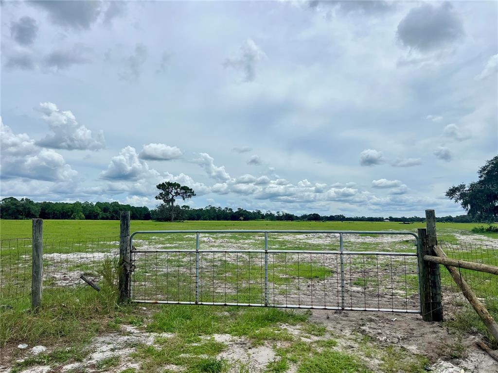 A metal gate stands at the entrance to a large, open, grassy pasture — ALTURAS BABSON PARK CUT-OFF, BARTOW, FL