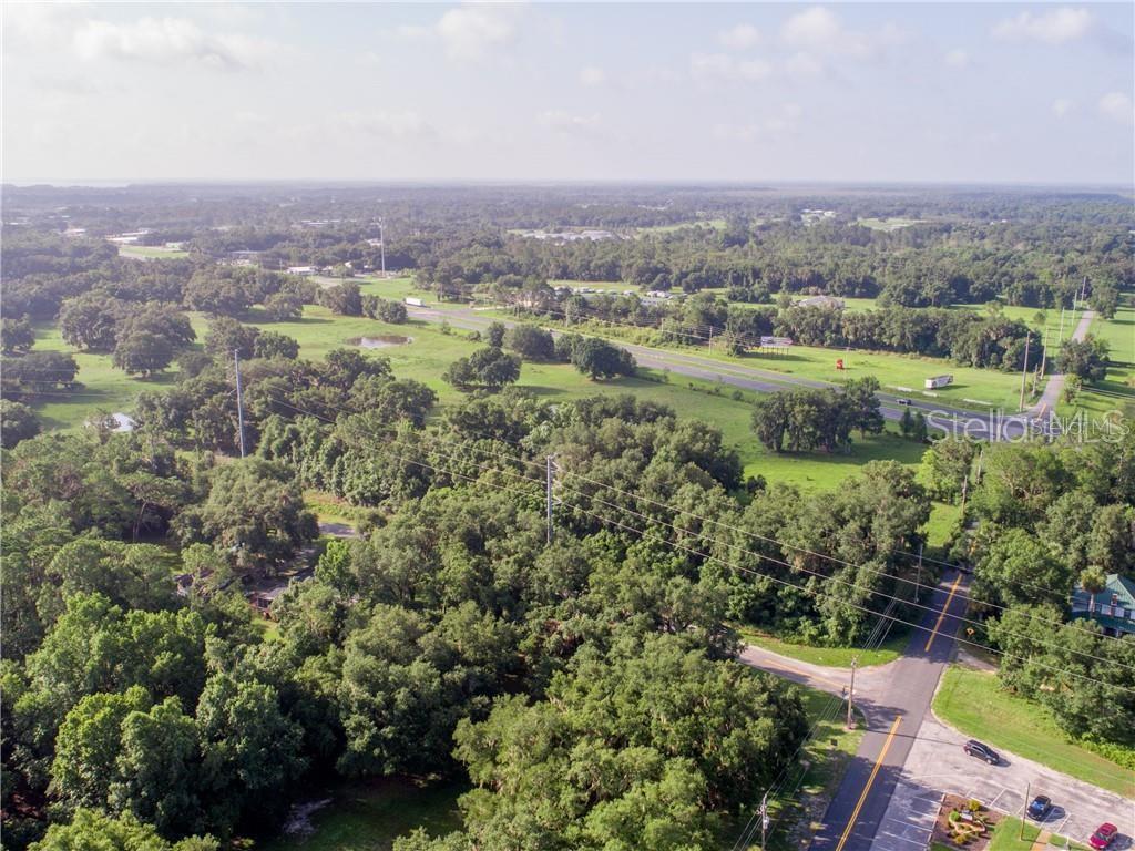 An aerial view shows a rural landscape with a road, dense trees, and open fields — 1315 SR 44, LEESBURG, FL
