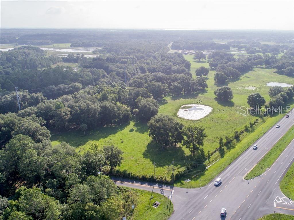 An aerial view shows a large, grassy plot of land with trees and a pond — 1315 SR 44, LEESBURG, FL