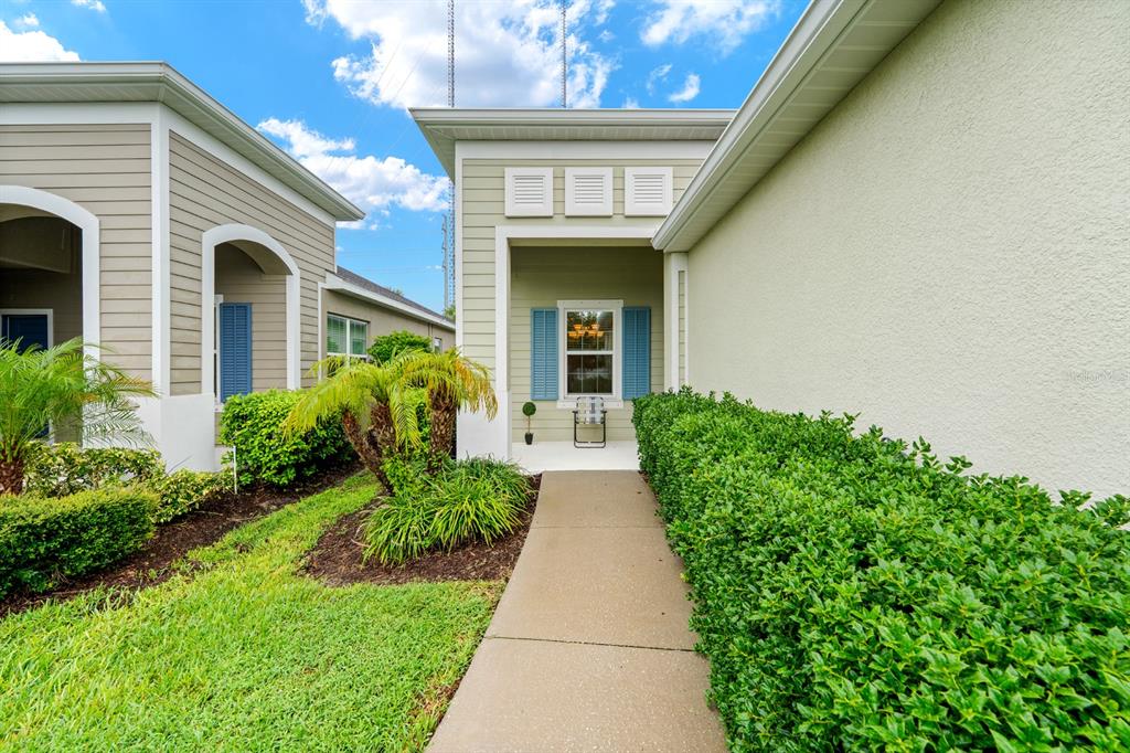 A concrete walkway leads to the recessed front entrance of a house with light-colored siding — 13542 CIRCA CROSSING DRIVE, LITHIA, FL