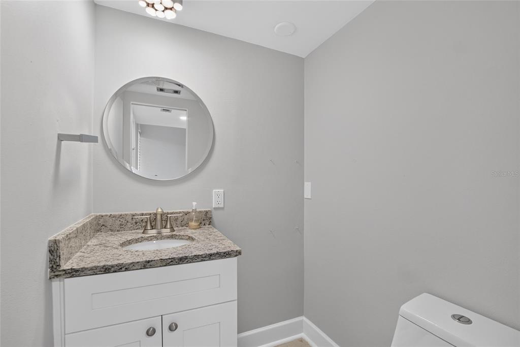 A bathroom features a granite vanity, a round mirror, and a white toilet — 1028 APOLLO BEACH BOULEVARD UNIT 11, APOLLO BEACH, FL