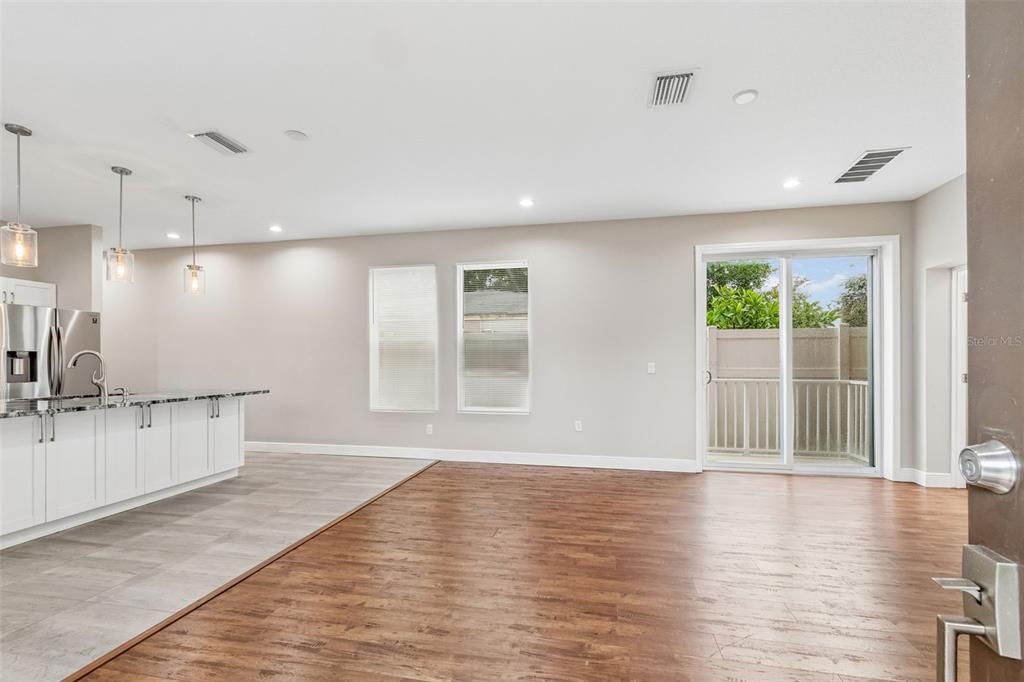 An open-concept kitchen and living area featuring wood-look flooring, white cabinetry, and a sliding door — 8528 PATSY STREET, TAMPA, FL