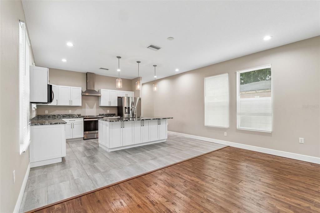 A kitchen with white cabinets, a granite island, and gray tile flooring next to wood flooring — 8528 PATSY STREET, TAMPA, FL