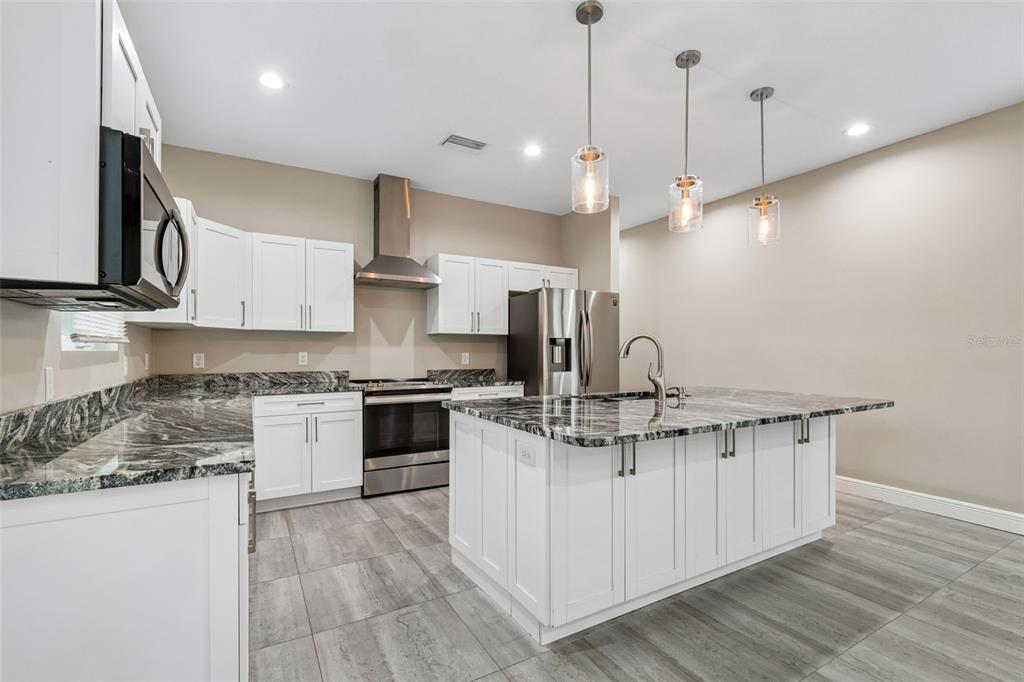 A kitchen features white cabinets, granite countertops, a center island, and stainless steel appliances — 8528 PATSY STREET, TAMPA, FL