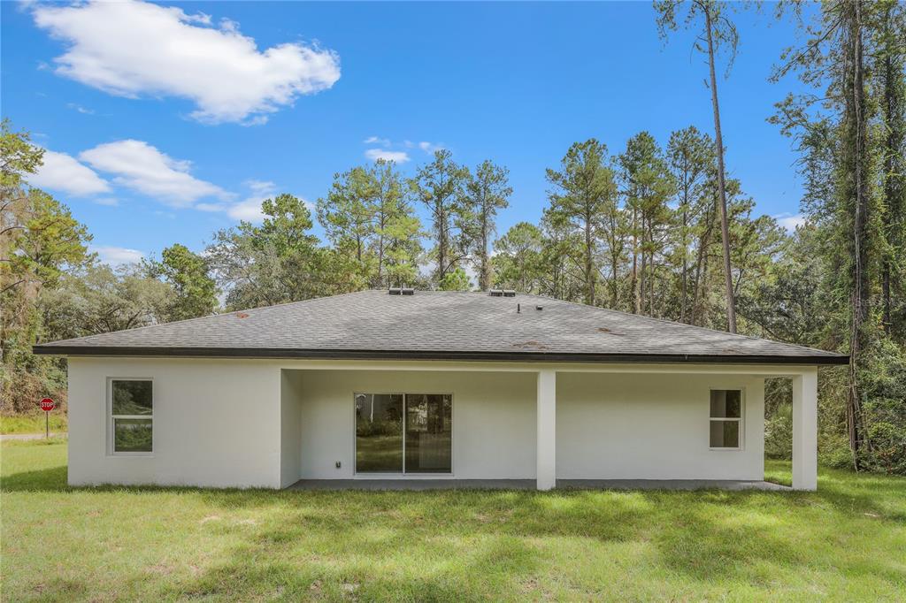 The rear exterior of a single-story white house features a covered patio and sliding doors — 14519 SW 79TH AVE RD, OCALA, FL