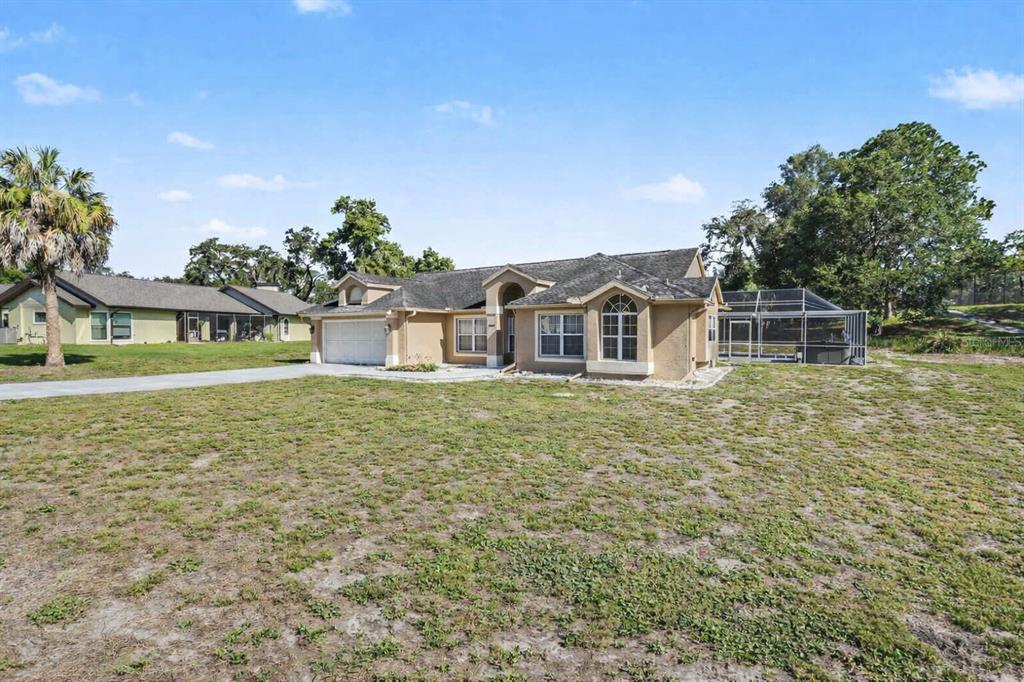 A tan single-story house with a garage and a screened-in pool area — 13037 EVERARD DRIVE, SPRING HILL, FL