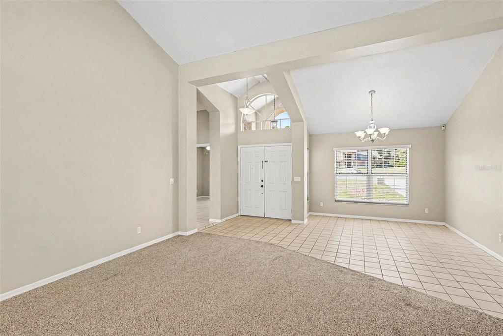 An entryway with tiled flooring transitions into a carpeted living area with high vaulted ceilings — 13037 EVERARD DRIVE, SPRING HILL, FL