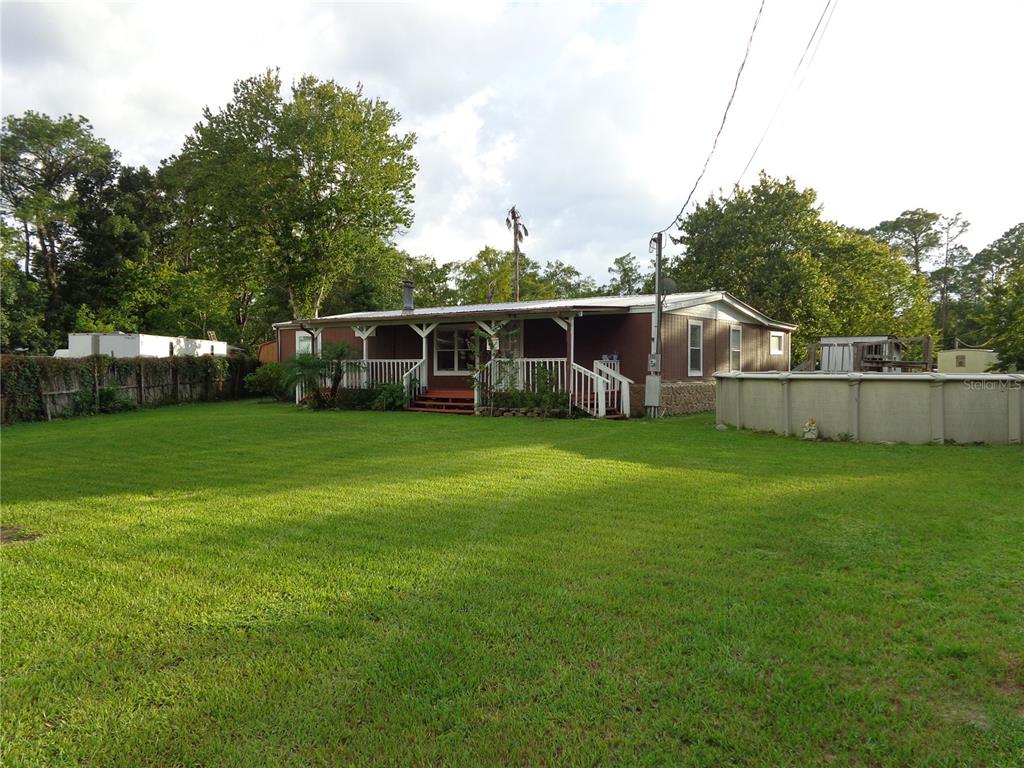 A brown manufactured home with a front deck and an above-ground pool in the yard — 135 SPORTSMAN ROAD, SATSUMA, FL