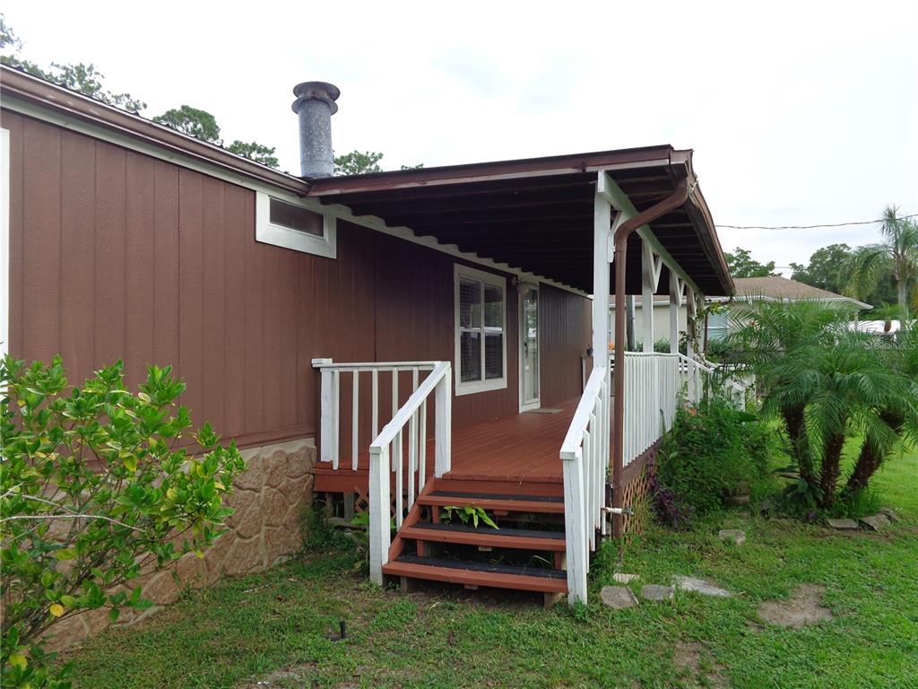 A brown mobile home features a covered wooden deck with white railings and stairs — 135 SPORTSMAN ROAD, SATSUMA, FL