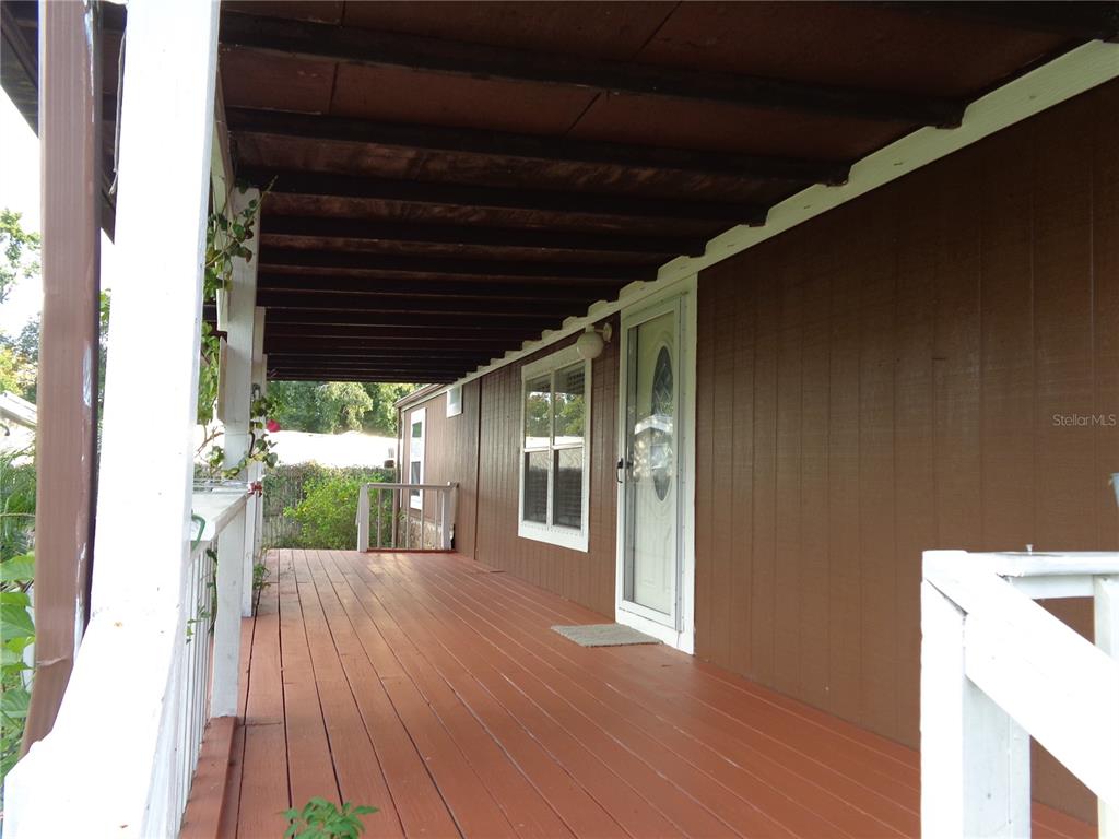 A long wooden porch with a white railing runs along the side of a brown house — 135 SPORTSMAN ROAD, SATSUMA, FL