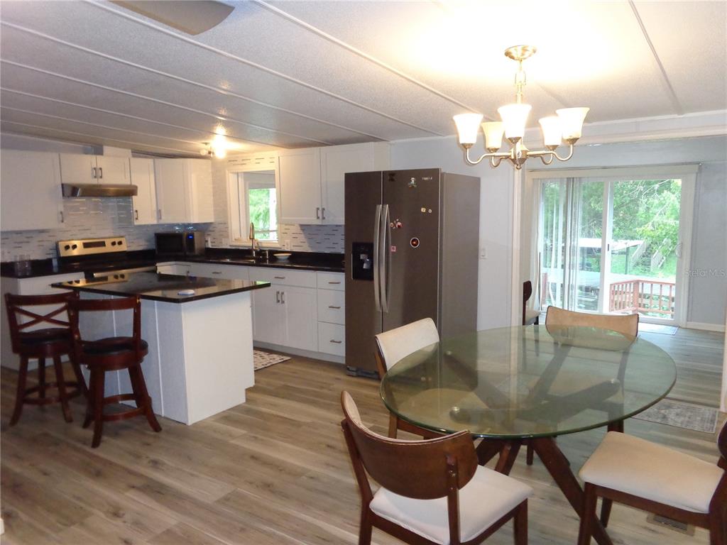 A kitchen and dining area featuring white cabinets, dark countertops, a glass table, and wood-look flooring — 135 SPORTSMAN ROAD, SATSUMA, FL