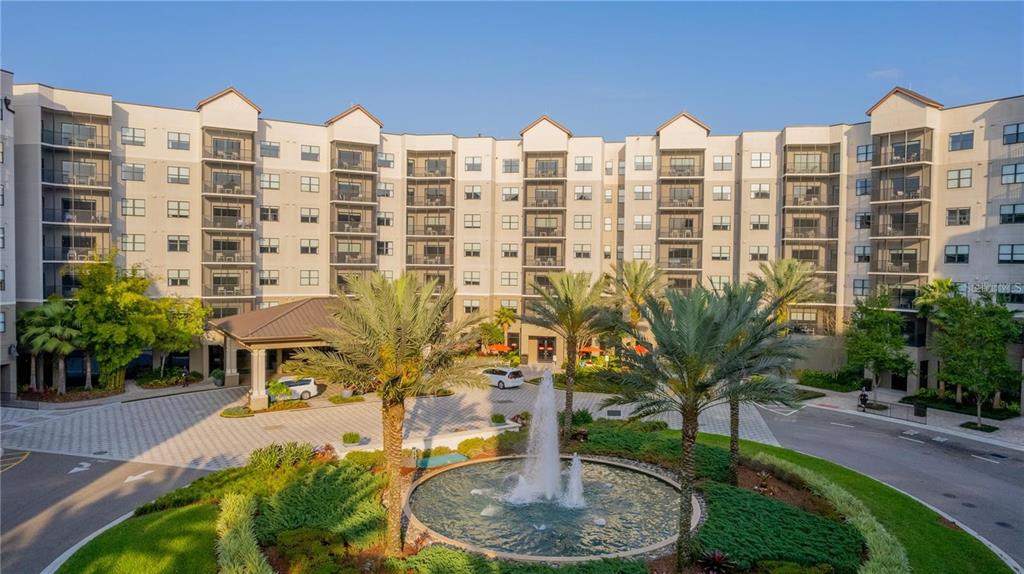 An exterior view of a multi-story apartment building with a circular fountain in the foreground — 14501 GROVE RESORT AVENUE UNIT 1310, WINTER GARDEN, FL