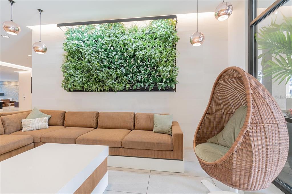 A modern lounge area features a large living plant wall, a brown sofa, and a wicker chair — 14501 GROVE RESORT AVENUE UNIT 1310, WINTER GARDEN, FL