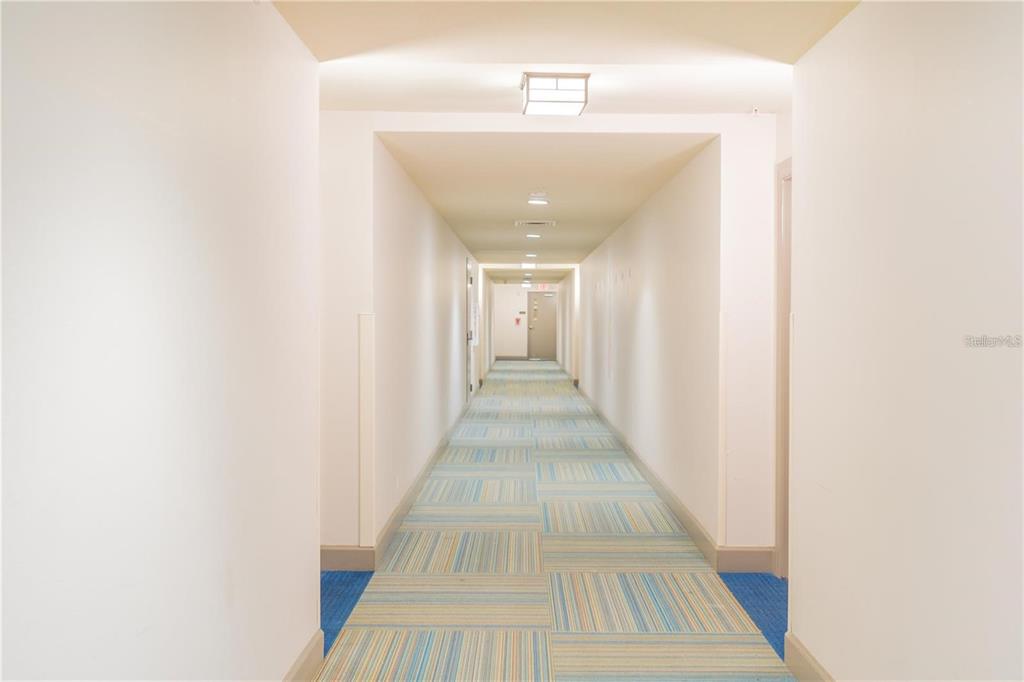 A long, narrow indoor hallway features white walls, recessed lighting, and blue-patterned carpeted flooring — 14501 GROVE RESORT AVENUE UNIT 1310, WINTER GARDEN, FL