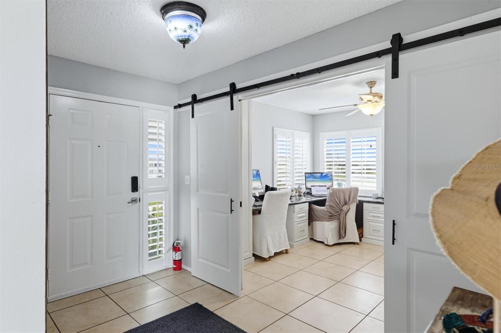 An entryway with tile flooring leads into a home office through white sliding barn doors — 1103 EDGEWATER CIRCLE UNIT 1103, BRADENTON, FL