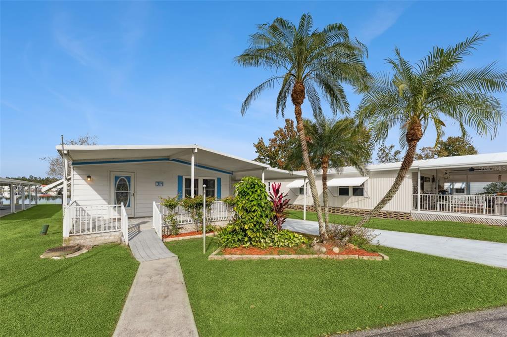 A white mobile home with a front porch, palm trees, and a concrete walkway — 314 LAKEVIEW DRIVE, OSTEEN, FL