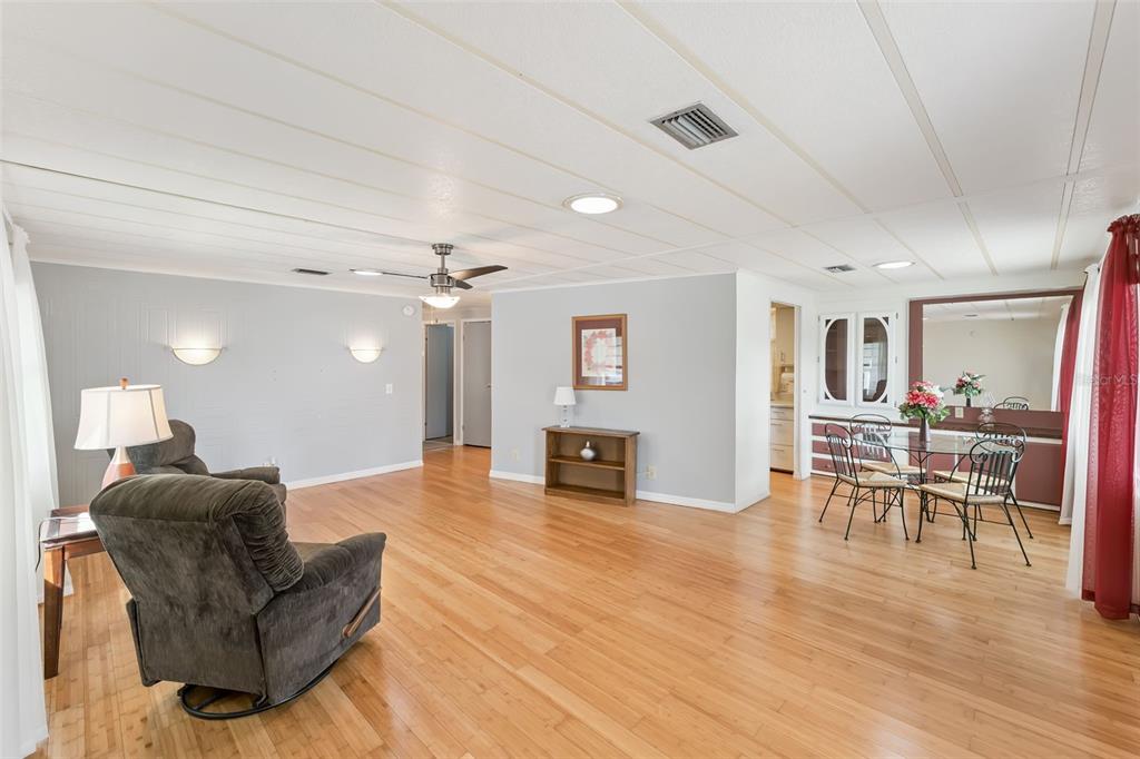 A spacious living and dining area with light wood flooring, gray walls, and a ceiling fan — 314 LAKEVIEW DRIVE, OSTEEN, FL