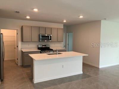 A modern kitchen features gray cabinets, a white island, and stainless steel appliances — 35694 KINSEY POINT, ZEPHYRHILLS, FL