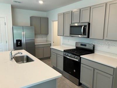 A modern kitchen features gray cabinets, stainless steel appliances, and a white quartz island countertop — 35694 KINSEY POINT, ZEPHYRHILLS, FL