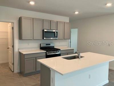 A modern kitchen features gray cabinets, stainless steel appliances, and a white quartz island countertop — 35694 KINSEY POINT, ZEPHYRHILLS, FL