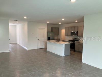 An open-concept kitchen features a center island, gray cabinetry, and light-colored tile flooring — 35694 KINSEY POINT, ZEPHYRHILLS, FL