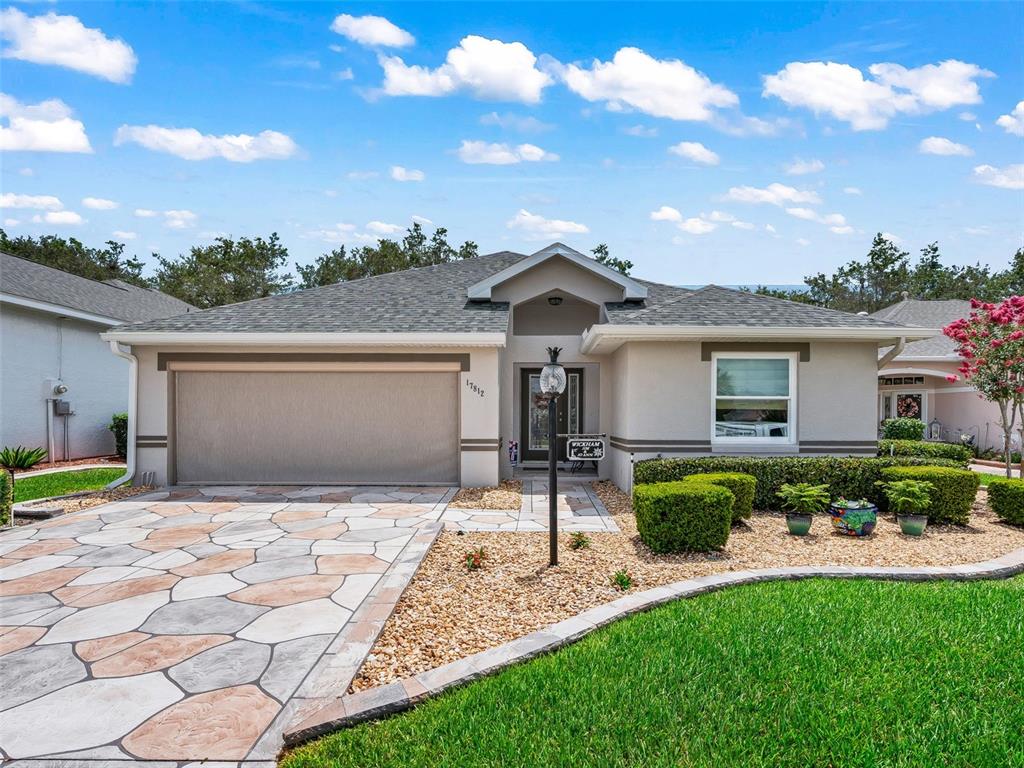 A single-story house features a patterned concrete driveway, a two-car garage, and landscaped front yard — 17812 SE 113TH TERRACE, SUMMERFIELD, FL