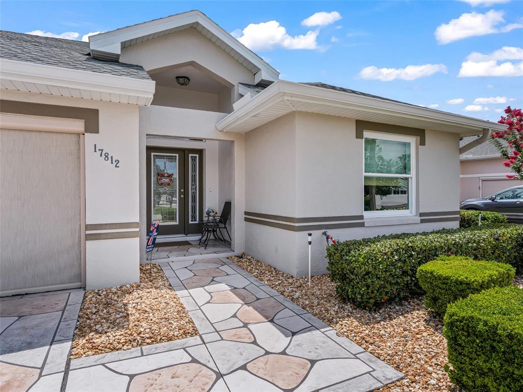 A beige house exterior features a stone-patterned walkway leading to a recessed front entrance — 17812 SE 113TH TERRACE, SUMMERFIELD, FL