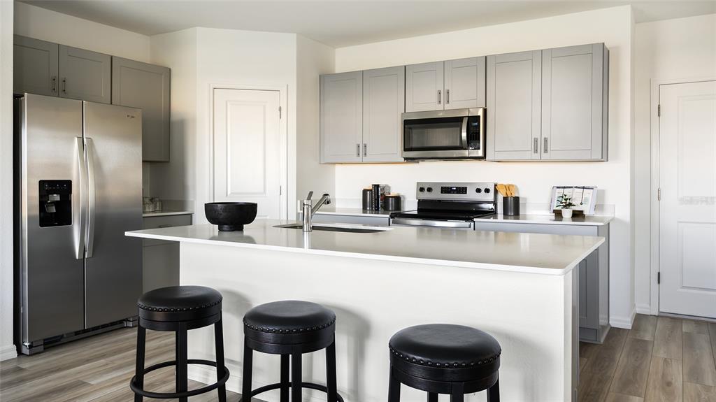 A modern kitchen features gray cabinets, stainless steel appliances, a white island, and bar stools — 5377 SAN PIETRO DRIVE, WINTER HAVEN, FL