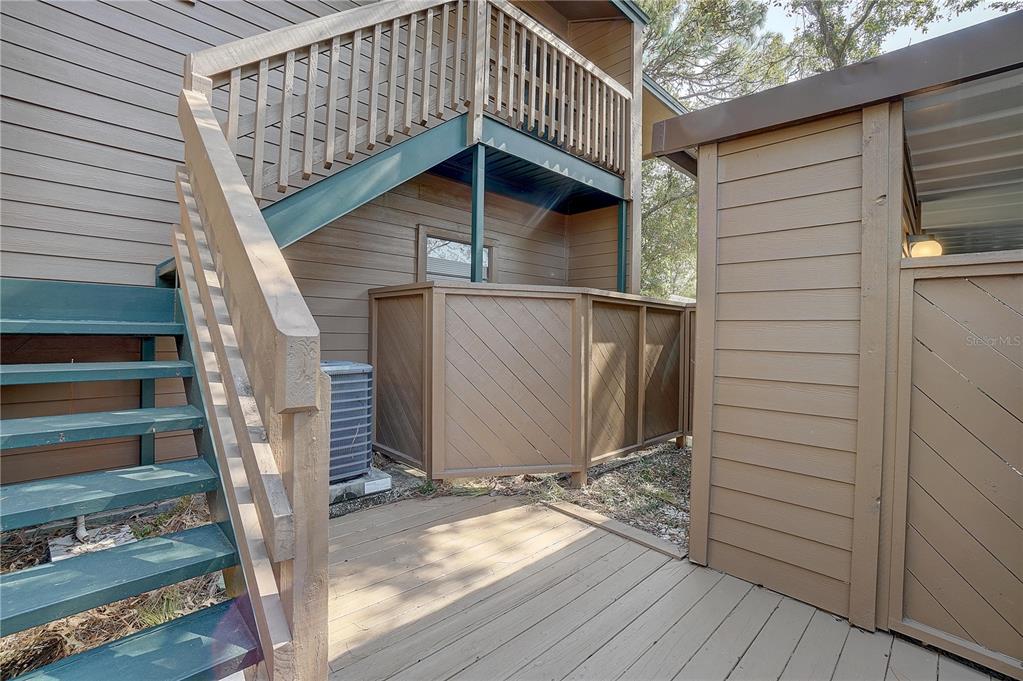 An exterior view shows a wooden staircase leading to a balcony above a ground-level deck — 1106 LENNOX ROAD W, PALM HARBOR, FL