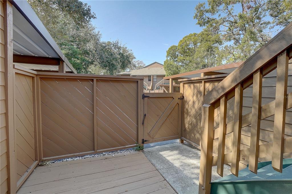 A wooden gate separates a small deck from a concrete walkway near an outdoor staircase — 1106 LENNOX ROAD W, PALM HARBOR, FL