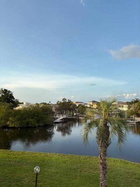 A sunroom features large windows overlooking a canal, a ceiling fan, and a potted plant — 4609 MARINE PARKWAY UNIT 203, NEW PORT RICHEY, FL