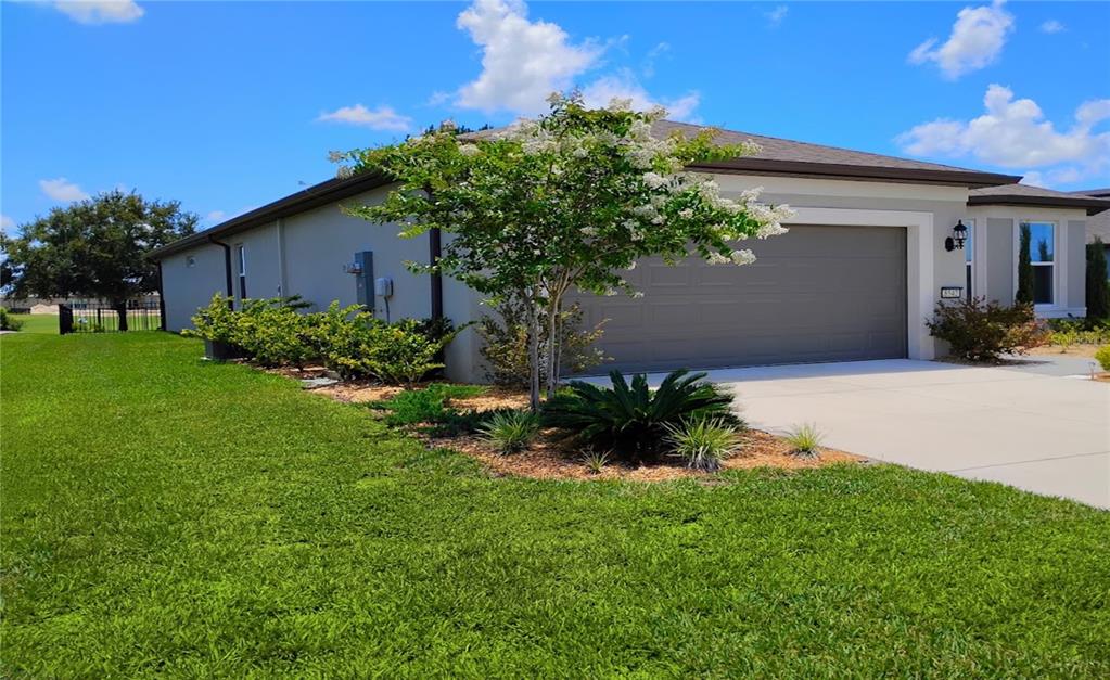 A single-story house exterior features a gray garage, a blooming tree, and a green lawn — 8542 SW 55TH STREET ROAD, OCALA, FL