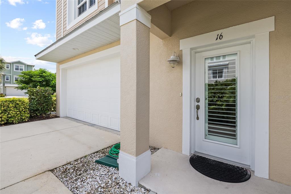 A beige house exterior features a white garage door, a front door with glass, and landscaping — 10311 LANDS END CIRCLE UNIT 16, PLACIDA, FL