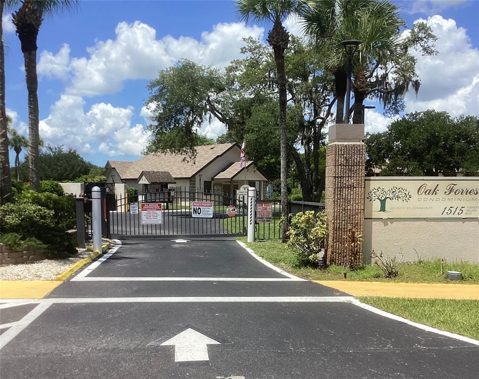 The entrance to a gated condominium community features a paved driveway, signage, and palm trees — 1515 FORREST NELSON BOULEVARD UNIT K106, PORT CHARLOTTE, FL