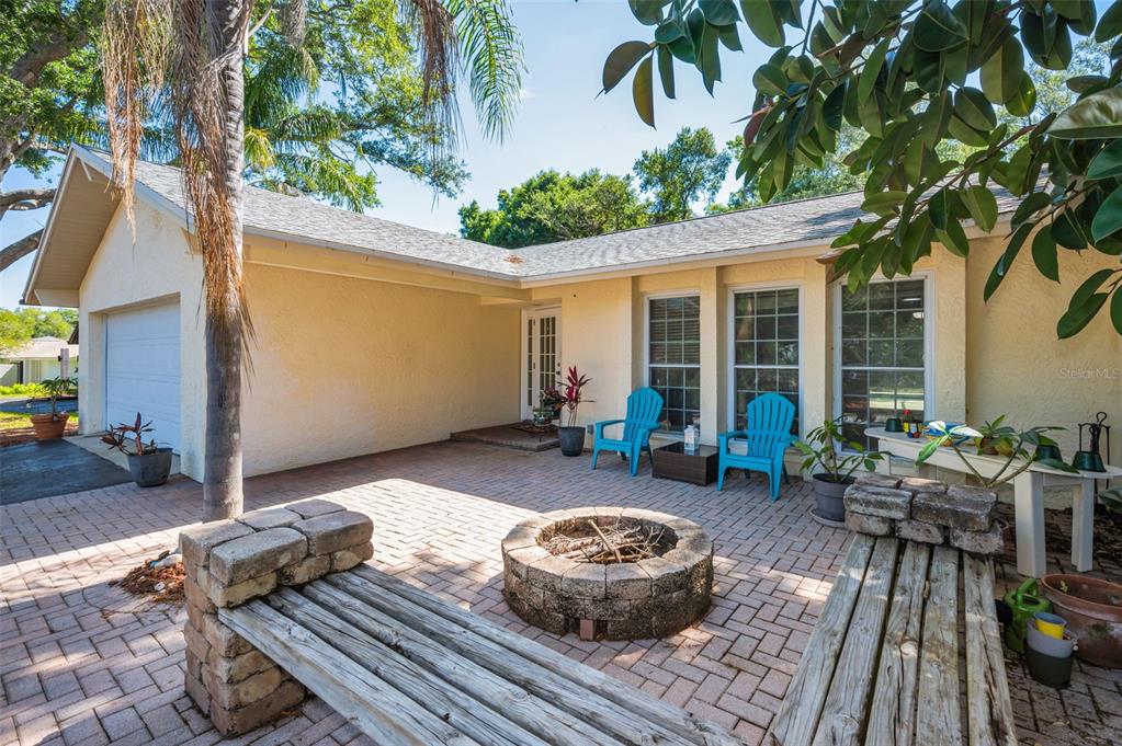 A paved patio features a stone fire pit, wooden benches, and two blue chairs — 520 SANDY HOOK ROAD, PALM HARBOR, FL