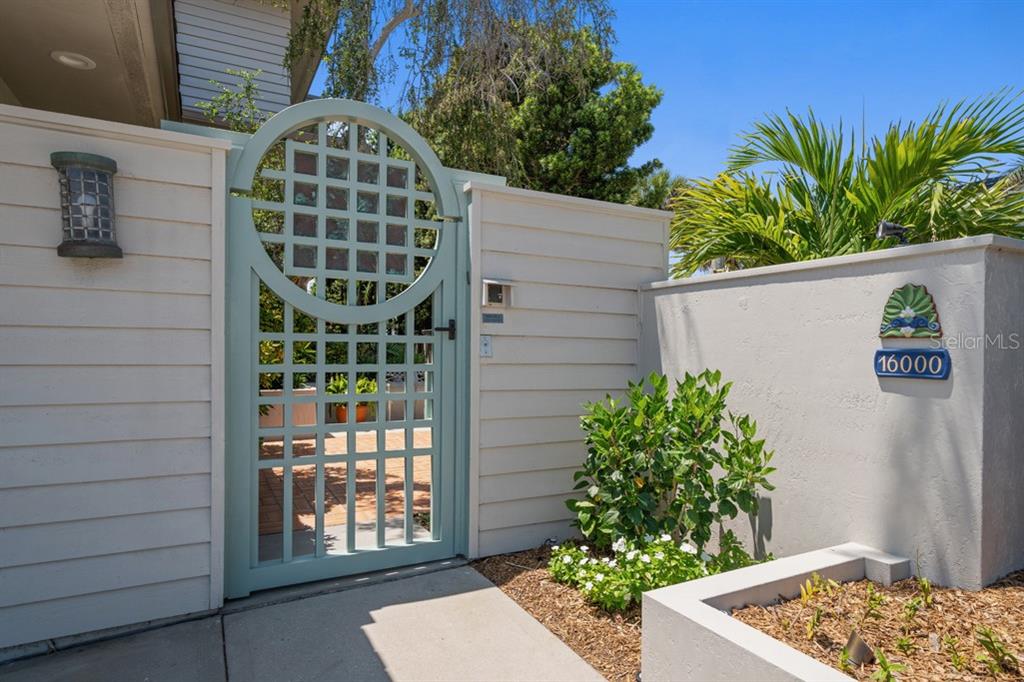 A light blue gate with a circular lattice design stands beside a white wall — 16000 GULF BOULEVARD, REDINGTON BEACH, FL