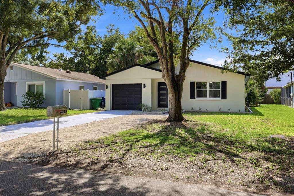 A single-story house with a white exterior, dark garage door, and a gravel driveway — 6413 S ENGLEWOOD AVENUE, TAMPA, FL