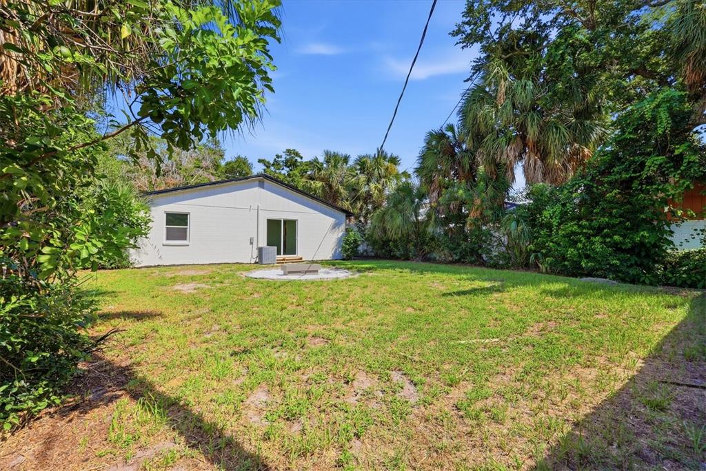 A white house with a sliding glass door sits behind a grassy backyard with trees — 6413 S ENGLEWOOD AVENUE, TAMPA, FL