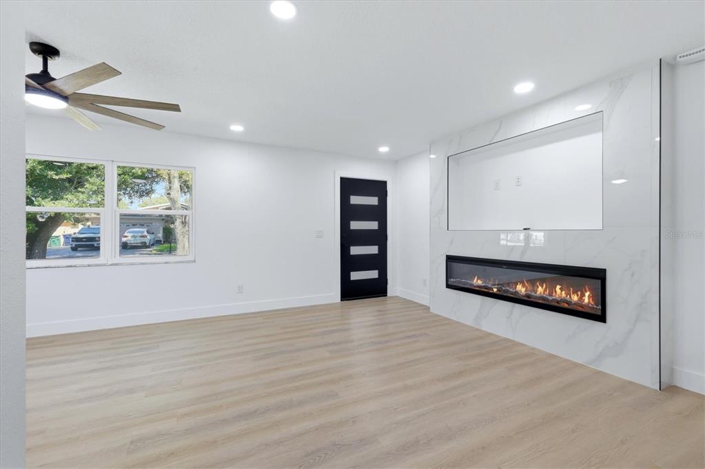 A living room features light wood flooring, a modern fireplace, and a black front door — 6413 S ENGLEWOOD AVENUE, TAMPA, FL