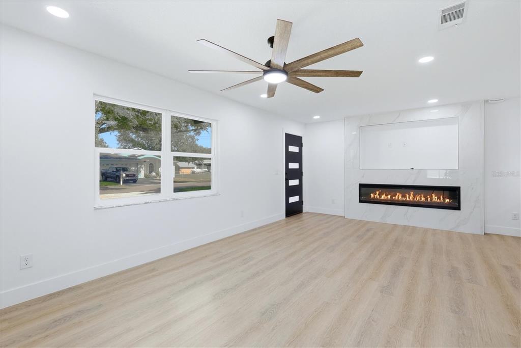 A bright living room features light wood flooring, a ceiling fan, and a modern fireplace — 6413 S ENGLEWOOD AVENUE, TAMPA, FL