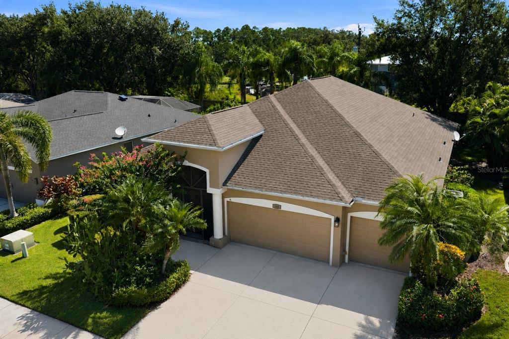 An elevated exterior view of a tan house with a three-car garage and shingled roof — 295 LONDONDERRY DRIVE, SARASOTA, FL