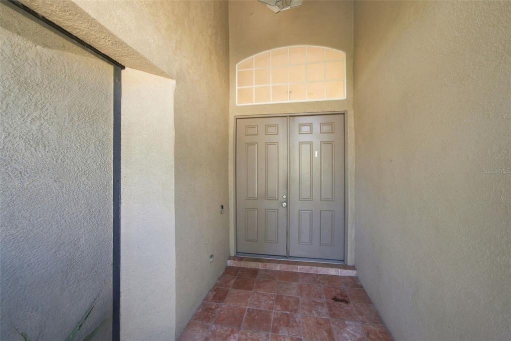 A double front door with a transom window sits under a covered entryway with tile flooring — 295 LONDONDERRY DRIVE, SARASOTA, FL